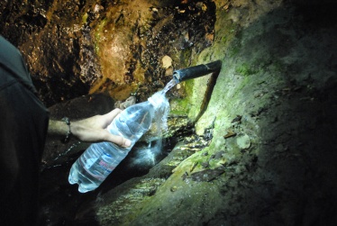 holding a water bottle illuminated by a headlamp to be filled by an artesinal mineral spring coming out of a rubber pipe stuck into the rock in Nagorno-Karabakh